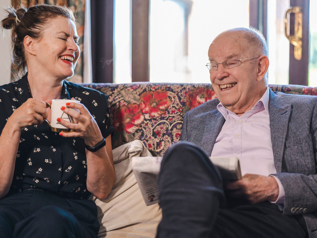 Ann and her father laugh together on a sofa