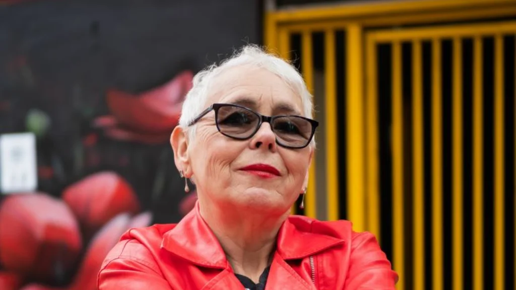 A woman in a red leather jacket against a graffiti background