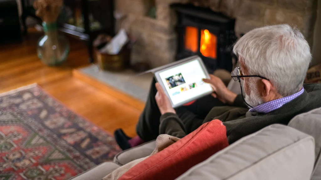 An abstract image looking over the shoulder of a man with silver grey hair, who is looking at an ipad.